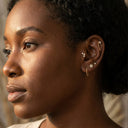 Close-up of a woman's ear with multiple earrings against a neutral background