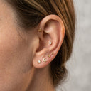 Close-up of an ear with gold earrings on a neutral background