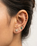 Close-up of an ear with multiple earrings including a green gemstone stud.