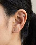 Close-up of an ear with gold earrings against a neutral background