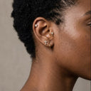 Close-up of an ear with multiple earrings on a neutral background
