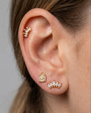 Close-up of an ear wearing gold earrings with a grey background
