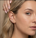 Close-up of a woman's ear with gold earrings against a neutral background