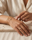 Close-up of a hand wearing gold jewelry on a neutral background wearing Ella and Faith London Jewellery