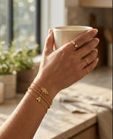 Hand holding a white mug with gold jewelry in a cozy indoor setting