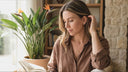 Woman sitting indoors with a plant and book in the background. wearing Ella and Faith London Jewellery