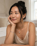 Woman wearing a Ella & Faith London necklace with a small pendant, sitting indoors.