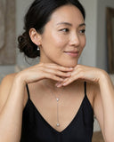 Woman wearing a delicate necklace and earrings in a neutral setting- Moissanite Drop Pendant Necklace worn on a model, showcasing its elegant design and sparkle.