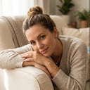 Woman in a beige sweater sitting on a couch in a cozy living room wearing Ella and Faith London Jewellery