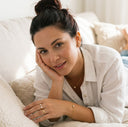 Woman sitting on a couch with a neutral expression, wearing a white shirt.