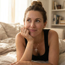 Woman sitting on a bed with a thoughtful expression, wearing Ella & Faith London jewellery.