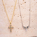 Two necklaces, one gold Crucifix and one silver angle wings on a textured beige surface.