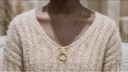 Person wearing a beige sweater and gold necklace with a circular pendant.