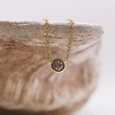 The Mini CZ Bracelet Gold  with a round pendant on a stone surface