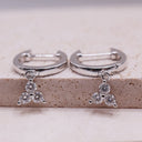 Mini Moissanite Drop Hoop Earrings- Three Stone Charm on a textured surface with sparkling moissanite stones.