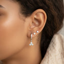 Mini Moissanite Drop Hoop Earrings- Three Stone Charm- Close-up of an ear wearing silver hoop earrings with small gemstones.