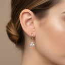Mini Moissanite Drop Hoop Earrings- Three Stone Charm- Gold earring with three clear stones worn by a person against a neutral background