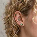 Close-up of an ear wearing green floral earrings with blonde hair.