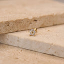 Flora CZ Flower Piercing Stud. A small gold stud earring with a five-pointed star design set with clear gemstones, resting on a beige stone surface.