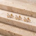 Three Flora Vine CZ Cartilage Studs with marquise-cut clear stones, arranged on beige stone steps.