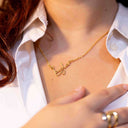 Person wearing a gold `Layla` necklace with a name pendant on a white shirt. Personalised Name Necklace – 18K Gold-Plated

Waterproof | Hypoallergenic | Made-to-Order