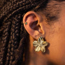 Model wearing gold sculpted floral stud earrings with layered gold jewellery.
