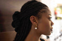Woman with braided hair wearing a pearl earring in a blurred indoor setting