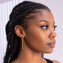 Woman with braided hair wearing a gold earring against a white background