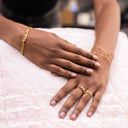 Hand with Twin Stone Sparkle Open Ring – Gold or Rhodium Plated on a blurred background- Close-up of a person's hands with gold jewellery on a white surface