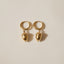 Pair of gold acorn hoop earrings on a beige background