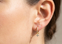 Close-up of an ear wearing a gold earring with a small gemstone on a neutral background