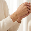 Gold Initial Bracelet- Stacked Gold bracelet with letters on a person's wrist against a neutral background