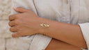 Gold bracelet with arrow design on a wrist against a neutral background