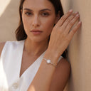 Halo Moissanite Bangle | 1ct VVS Moissanite | 925 Sterling Silver. A woman wearing a delicate silver bangle bracelet with a round pavé-set clear stone, posing against a textured beige wall.
