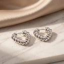 Ayra Twist Hoop Earrings -Pair of silver hoop earrings on a beige fabric background