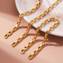 Three Elara Link Bracelets with lobster clasp ends, arranged diagonally on a light pink surface next to a white marble plate.