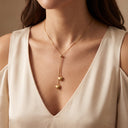 Adora Heart Lariat Necklace- A close-up of a model wearing a delicate gold lariat necklace with two dangling heart charms, styled with a cream-colored satin top.