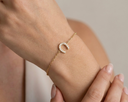 Gold bracelet with a horse shoe charm on a wrist against a neutral background