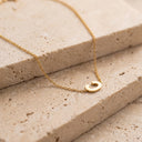 Gold Initial Bracelet- A delicate gold chain necklace with a small, polished gold initial 'C' pendant, displayed on textured beige stone blocks.