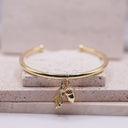 Acorn & Oak Leaf Open Bangle Gold bracelet with acorn and leaf charm on a textured surface