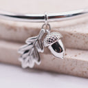 Acorn & Oak Leaf Open Bangle Silver bracelet with acorn and leaf charms on a wooden surface
