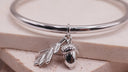 Silver bangle with acorn and leaf charm on a beige background
