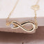 Gold infinity necklace with a small diamond on a beige surface