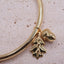 Gold bangle with acorn and leaf charm on a light pink background