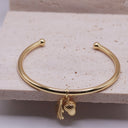 Acorn & Oak Leaf Open Bangle Gold bracelet with acorn and leaf charm on a textured surface