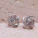 Silver knot earrings with clear stones on a beige surface