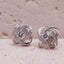Silver knot earrings with clear stones on a beige surface