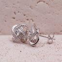 Silver earrings with a diamond on a textured beige surface