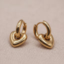 Gold-toned hoop earrings with a polished, organic curved bead-like accent, displayed on a textured light beige surface.