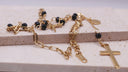 Adjustable clasp on Rosario beaded cross necklace- A gold-toned rosary necklace with black beads and a gold cross, displayed on a light beige stone block.